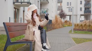 Genç bir kadın saçını ve şapkasını düzeltmek için akıllı telefonunun ön kamerasını ayna olarak kullanıyor. Video konferansına hazırlanıyor ya da sosyal medya için selfie çekiyor..