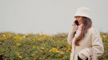 Yüzünde şaşkın bir bakışla kafası karışmış bir kadın bir telefon konuşmasını dinlerken göz kırpıyor. Serin bir sonbahar gününde dışarıda dikiliyor, konuşmadan beklenmeyen haberleri işliyor..