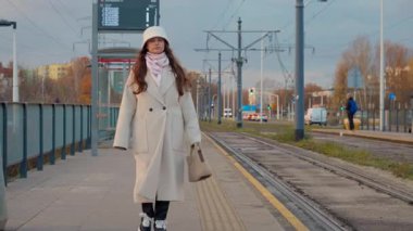 Kışlık paltolu ve şapkalı bir kadın akşam boyunca şehirde bir tramvay peronunda yürüyor. Kentsel ortam toplu taşımacılık, günlük ulaşım ve kentsel yaşamın anlarını yakalıyor.