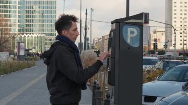 Otomatik self servis terminalinde kredi kartıyla park sayacı ödemesi. Şehir caddesinde bir adam hızlı bir elektronik işlem yapar arabasının park ücretini ödemek için..
