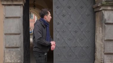 Endişeli bir adam tarihi bir kapının önünde beklerken gergin bir şekilde saatini kontrol eder. Sabırsız ya da hayal kırıklığına uğramış görünüyor. Buluşmaya ya da randevusuna geç kalan birini arıyor..