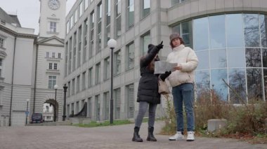 Genç bir kadın eşinin yön bulmasına yardım eder, haritayı gösterir ve bir dönüm noktasına doğru hareket eder. Yol arkadaşı, tarihi mimariyle çevrili bir caddedeki güzergahı anlatırken şaşkın görünüyor..