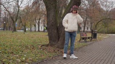Genç bir adam soğuk bir sonbahar gününde halka açık bir parkta akıllı telefonunu iletişim kurmak için kullanıyor. Bir yolda duruyor, cep telefonuyla konuşuyor gelişi koordine etmek için..