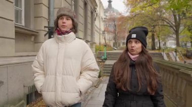 Genç bir çift, sonbaharda bir Avrupa kentinde yürürken sakin bir sohbetin tadını çıkarıyor. Yakın etkileşimleri, bağlarını ve şehir gezintisinde birlikte vakit geçirmenin zevkini vurguluyor..