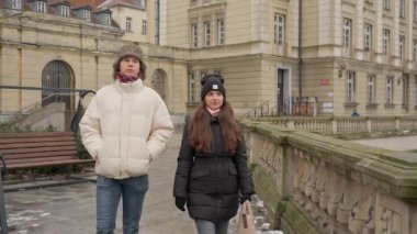 Genç bir adam ve bir kadın kışın bir şehir parkında rahatlatıcı bir yürüyüşün tadını çıkarıyorlar. Bir bankın ve salıncağın yanından geçerek klasik mimarinin arka planına karşı huzurlu bir anı paylaşıyorlar..