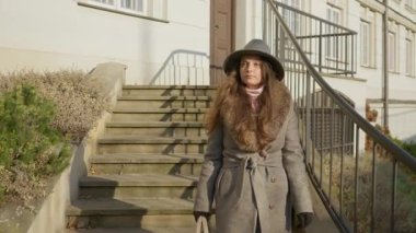 Şık bir ceket ve şapka giyen zarif bir kadın taştan merdivenlerden şehir caddesine doğru yürüyor. Polonya 'nın başkenti Varşova' da güneşli bir günde yayalar eşliğinde şehir hayatı sahnesi.