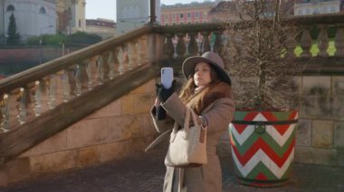 Genç bir kadın turist, blogcu veya içerik yaratıcısı, tarihi bir dönüm noktasının fotoğraflarını çekmek veya video kaydetmek için cep telefonunu kullanıyor. Varşova 'da sosyal medyada seyahat anılarını paylaşmak.