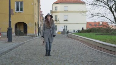 Sıcak bir palto ve şapka giyen şık bir kadın soğuk, bulutlu bir sonbahar ya da kış gününde tarihi bir şehirde yürüyor. Bir melankolik ve atmosferik Avrupa şehir manzarası.