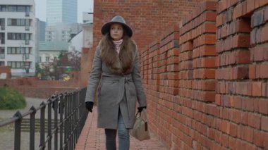 Bir kadın, Varşova 'da tarihi bir ortaçağ duvarı boyunca yürüyor ve arka planda modern şehir gökdelenleri görülüyor. Geçmiş ve şimdiki zaman arasındaki bir zıtlık kavramı.