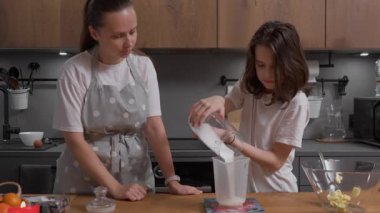 Bir çocuk dijital ölçekte bir ölçü kabına şekeri dikkatlice dökerek annesinden pişirmeyi öğrenir. Bir ebeveyn çocuğa tarifi takip etmeyi ve ev yapımı hamur işi malzemelerini ölçmeyi öğretir..