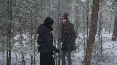 Anne ve oğlu karlı bir ormanda kış yürüyüşüne çıktılar. Ebeveyn, sürpriz bir kar yağışı yaratmak için bir ağaç dalını sallayarak eğlenceli bir şaka yapıyor. Mutlu aile dışarıda birlikte oynuyor ve gülüyor..