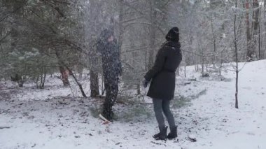 Bir çocuk, karla kaplı bir ağaç dalını sallayarak anneleri için kar sağanağı yaratıyor. Mutlu ebeveyn, etraflarında kar yağarken kahkahalar atarak eğlenmeyi sever. Neşeli bir aile Kış gününün tadını çıkarıyor.