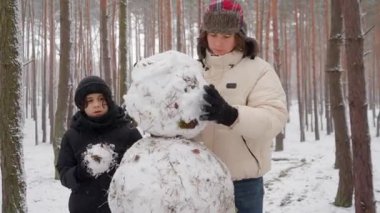 İki kardeş, ağır kartopunu kaldırmak için takım olarak çalışıyor. Başı dikkatlice gövdenin üstüne yerleştirirler ve kardan adamlarının ana yapısını kış ormanlarında tamamlarlar..