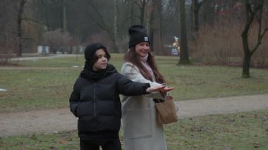 A mother and son share a heartwarming moment of bonding in an autumn park. A small, trusting blue tit bird eats seeds from the woman's hand while the boy watches closely in amazement.