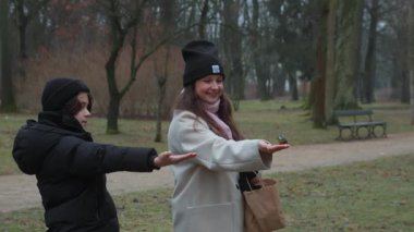 Bir anne ve oğul, sonbahar yürüyüşü sırasında iki evcil meme faresi kuşunu doğrudan ellerinden besleyerek neşeli bir anı paylaşırlar. Doğayla bağlantılı eğlenceli ve keyifli bir aile aktivitesi..