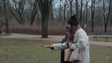 Bir anne sonbahar parkında eğlenceli bir aile aktivitesi düzenliyor oğluyla bir grup evcil meme faresini besliyor. Güvenen kuşlar tohumlarını yemek için iki ellerine de uçarlar..