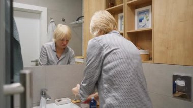 Olgun kadın banyoda günlük cilt bakımını yapıyor. Yüz toneri ya da losyonu temizlik, yaşlanma karşıtı etkiler ve taze ve sağlıklı bir cilt için pamuk pedi ile uyguluyor..