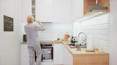 Son sınıf öğrencisi bir kadının şık, aydınlık bir mutfakta sabah rutinine başlaması. Bu ev içi sahne, günlük yaşam ve yaşam tarzı kavramları için mükemmel bir iç mekan..