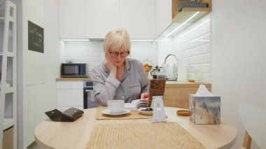 Gözlüklü, emekli bir beyaz kadın evde entellektüel hobisinin tadını çıkarıyor. Bir roman okuyor ve sıcak bir içecek içiyor. Günlük yaşamında dinginlik ve dijital detoks anı..