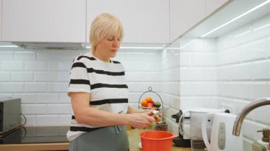Yaşlı bir kadın mutfağında bir elmayı küçük parçalara ayırıyor. Olgun bayan ev yapımı turta ya da turta için taze meyve malzemesi hazırlıyor. Geleneksel bir tatlı tarifi hazırlıyor..