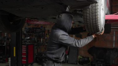 Tamircinin biri araba servisi atölyesinde araç süspansiyon sorunu teşhis etti. Bir teknisyen tamir için kaldırılan bir arabanın eski bir top eklem yerini belirlemek için tekerlek oyununu kontrol ediyor..