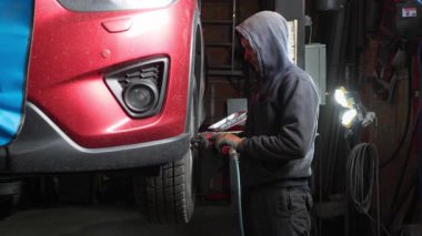 Garajdaki oto tamircisi asansördeki tekerleği sökmek için basınçlı anahtar kullanır. Profesyonel teknisyen süspansiyon onarımı veya mevsimlik lastik ve araç bakımı yapar.