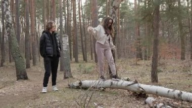 Genç bir çift ormanda eğlenceli bir yürüyüşün tadını çıkarıyor. Bir kadın düşmüş bir kütüğün üzerinde denge kuruyor, bir erkek izlerken koordinasyonunu test ediyor. Gençler için açık hava aktivitesi ve birliktelik anı