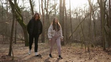 Altın yapraklı bir sonbahar ormanı, yolda yürüyen genç bir çift için manzaralı bir zemin sağlar. Erkek ve kadın, gün batımının sıcacık olduğu güzel bir günde doğada romantik bir yürüyüşün tadını çıkarırlar..