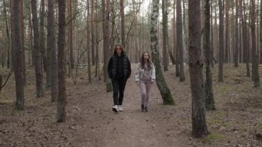 Ciddi bir ifadeye sahip genç bir çift yoğun, atmosferik bir ormanda kameraya doğru yürüyor. Bir erkek ve kadının yolculukta olduğu düşünceli ve karamsar bir sahne..