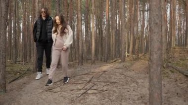 Genç ve mutlu bir çift ağaçların kökleriyle dolu bir patikada yokuş aşağı yürüyor. Kadın gülümsüyor ve konuşuyor. Çam ormanlarında gezintiye çıkarak engebeli arazide dikkatle geziniyorlar..
