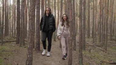 Genç bir çift güzel bir çam ormanında rahatlatıcı bir yürüyüş yapar, temiz hava alır ve sakin doğanın tadını çıkarır. Basit bir eğlence, eğlence ve refah anı..