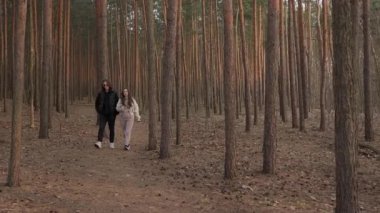 Genç bir çift, altın bir saatin günbatımının ılık ışığında, güzel bir çam ormanında yürür. Kadın konuşuyor ve işaret ediyor. Partneriyle mutlu bir anı paylaşıyor..