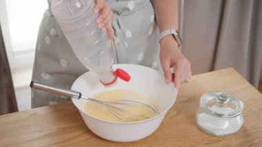 Bir kadın plastik bir şişeden yumurta hamuru ile birlikte bir kaseye süt döküyor. Ev yapımı bir kahvaltı hazırlama süreci, ev mutfağında yapılan bir yemek tarifinin ardından.