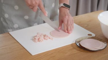 Bir ev hanımı dilimlenmiş jambonu beyaz bir kesme tahtasıyla keskin bir bıçakla doğruyor. Lezzetli bir omlet kahvaltısı için malzemeler hazırlıyorum. Protein zengini bir yemek için etli bir tarif..