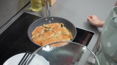 Bir aşçı tavuk göğsünü çubuksuz tavada kızartır, altın kahverengi eti spatulayla çevirir. Tavayı kapakla kaplayan, indüksiyon sobasında kümes hayvanları pişirme işlemi..