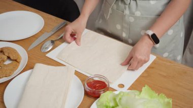 Bir aşçı ev yapımı shawarma hazırlar ve lavaş üzerine domates sosu sürer. Bir tavuğu sarma işlemi, kesme tahtasının içini doldurmak için temel oluşturur..