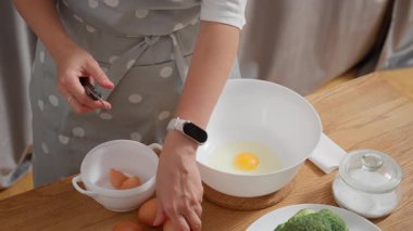 Dişi eller çiğ yumurtaları bir kaseye kırıyor. Bir ev hanımı brokolili kiş için malzemeler hazırlar, ev mutfağında sağlıklı bir kahvaltı hazırlar veya ev yapımı bir yemek pişirir..