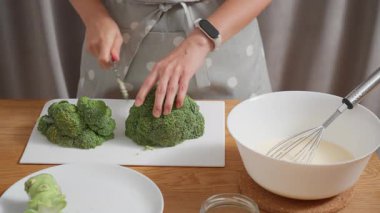 Bir kadın mutfak bıçağıyla beyaz bir kesme tahtasıyla taze yeşil brokoli doğruyor. Yemek hazırlama, sağlıklı bir vejetaryen yemeği pişirme ya da taze sebzelerle diyet yapma süreci..