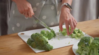 Kesme tahtasında taze brokoli doğramak. Bir kadın sağlıklı bir yemek hazırlamak için malzemeleri hazırlar. Vejetaryen diyeti, vejetaryen yaşam tarzı ve taze organik sebzelerle yemek pişirme kavramı..