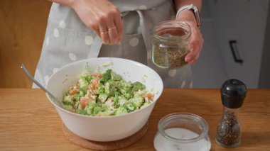 Tadına bakmak için somon ve brokoli sosu. Bir kadın karışıma tuz, biber ve kurutulmuş otlar ekler. Ev yapımı bir tarife tat ve baharat eklemenin son adımı..