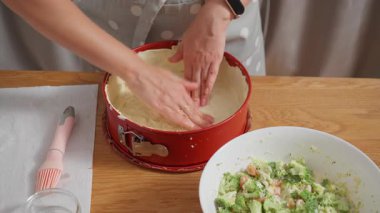 Pasta hamurunu kırmızı bir tavaya sıkıştırmak. Bir kadın ev yapımı kiş için kabuk ya da temel oluşturur. Lezzetli bir tart kabuğu ya da turta kabuğu yapma süreci..