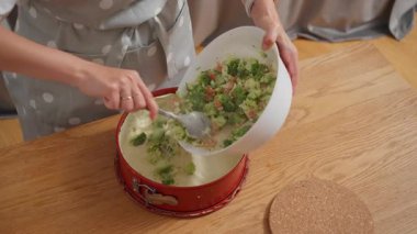 Lezzetli bir dolguyu hazır hamur kabuğuna döküyorum. Bir kadın ev yapımı somon ve brokolili kiş yapıyor. Pastayı fırında pişirmeden önce bir tarifin son adımı..