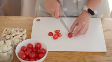 Beyaz bir kesme tahtasındaki bıçakla taze domatesleri ikiye bölmek. Bir kadın lezzetli ev yapımı pizza ya da pinsa sosu için sağlıklı sebze malzemeleri hazırlar. İtalyan yemeği pişirmek..