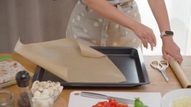 Ev yapımı pinsa için fırın örtüsü hazırlıyorum. Bir kadın parşömen kağıdını keser ve buruşturur, sonra pişirmeden önce metal bir tepsiye koyar. Mutfak fırını ve ev yapımı pişirme süreci.