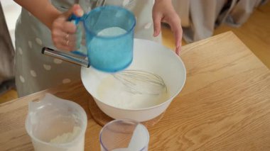 Un, elek ile doğrudan hamuru havadar yapmak için bir kaseye saplanıyor. Bir kadın ev yapımı kek ya da krep için hamur hazırlar ve karışıma özenle kuru malzemeyi ekler..