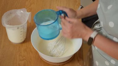 Pasta için ev yapımı hamur yapma süreci. Bir kadın unu bir kaseye yerleştirir ve hamuru çırpıcıyla karıştırır. Kahvaltıda lezzetli bir hamur işi yapmak için bütün malzemeleri birleştirir..