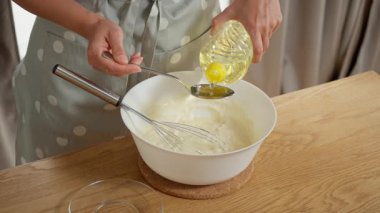 Esneklik ve nem için hamura sebze yağı ekliyorum. Bir kadın ev yapımı krep ya da krep için hamura bir kaşık ayçiçeği yağı döker ve bir kâseye koyar..