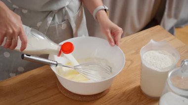 Bir kadın taze sütü yumurta ve şekerle bir kaseye dolduruyor, sıvı malzemeleri çırpıcıyla karıştırıyor. Ev yapımı krep, krep ya da turta için ince bir hamuru hazırlama süreci.