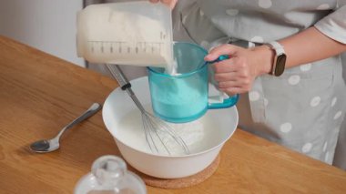 Bir kadın, buğday ununu süzgeçten geçirip direkt olarak sıvı hamurla bir kaseye koyar. Ev yapımı kek, pasta veya diğer hamur işleri için pürüzsüz, yumru yumru olmayan hamur hazırlama süreci.