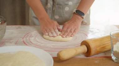Bir kadın fırıncı yapışkan hamurla çalışmak için silikon bir hasırın tozunu alır. Eller, ev yapımı ekmek veya pizza için taze bir hamur işi tabanı yapmak için ahşap bir merdane kullanır..